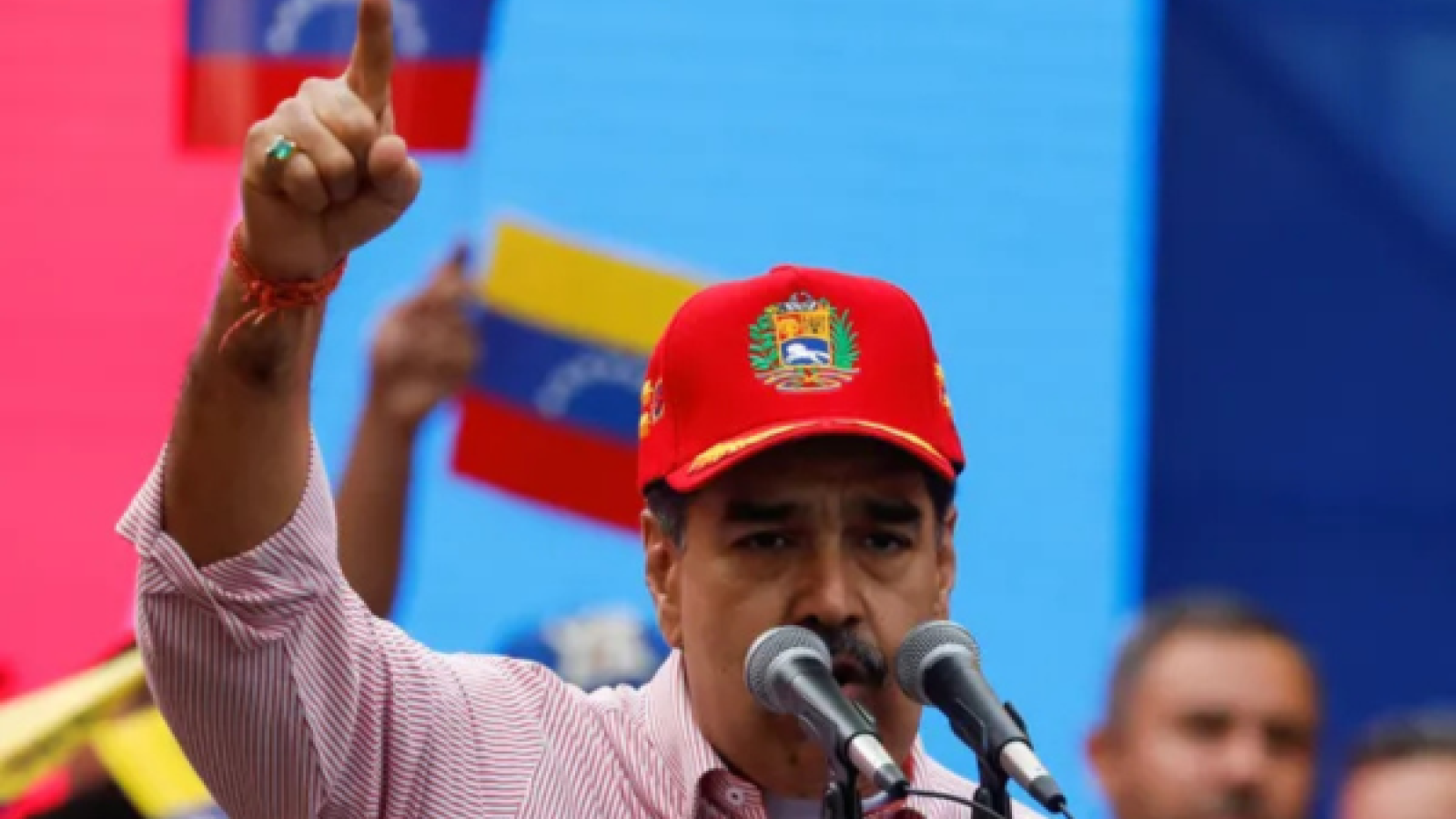 Man in baseball hat at podium holding up one arm